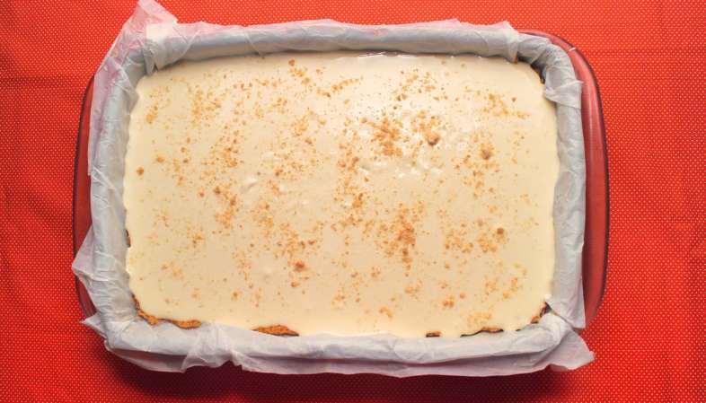 Nosso cheesecake na forma forrada com papel manteiga e pronto para ir ao forno com um pouco do farelo de bolacha Maizena por cima