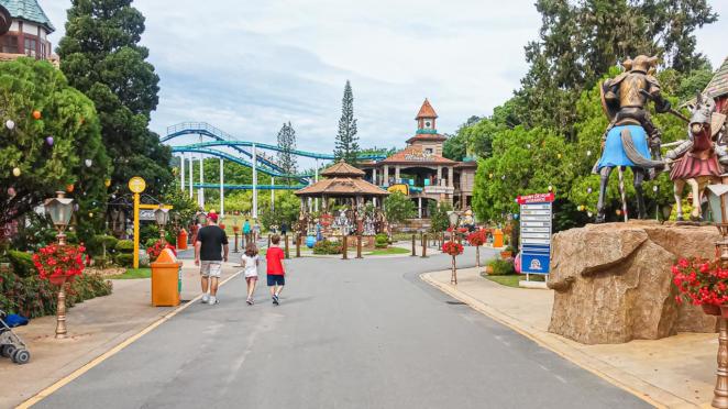 Beto Carrero World - Vila Germânica uma das áreas temáticas do parque à esquerda, pai e dois filhos caminham em direção a uma montanha-rusa, enquanto à direita vemos uma escultura de dois cavaleiros em combate