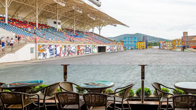 Beto Carrero World - Vista do restaurante para o Show Velozes e Furiosos No primeiro plano, mesas e cadeiras do restaurante estão em frente a uma proteção de vidro, ao fundo a pista onde é realizado o show e a arquibacanda