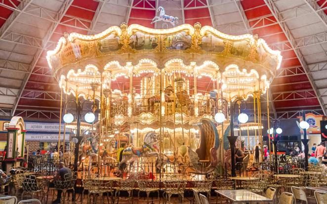 Beto Carrero World - Carrossel Veneziano na praça de alimentação do parque Um grande carrossel com ares antigos e totalmente iluminado com várias pequenas lâmpadas gira em meio a mesas e cadeiras da praça de alimentação